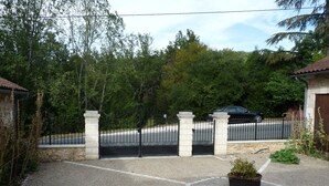 Uma entrada com portão leva a uma casa com muro de pedra e um carro preto estacionado no interior.