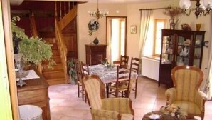 Uma área de refeições com uma escadaria de madeira, uma mesa de jantar posta com cadeiras, e uma cadeira decorativa com uma mesinha lateral.
