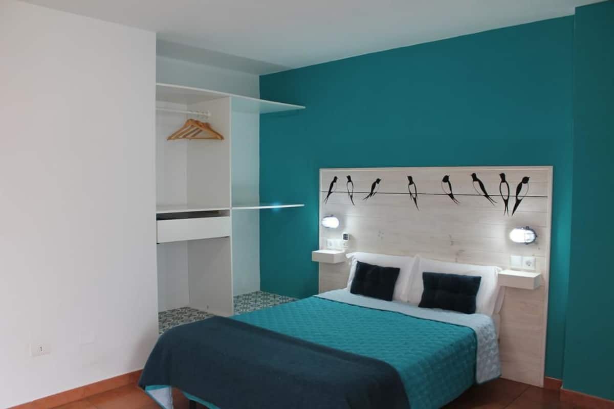 Un dormitorio con una cama, una mesita de noche, un estante en la pared y una obra de arte en la pared.