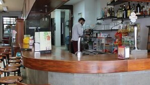 A bar area with a curved wooden counter, stools, and a person working behind the bar. - Hotel El Pino (Teror)