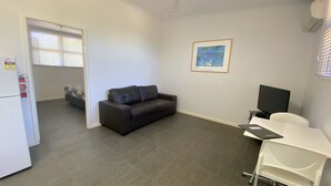 A compact living space with a sofa, a desk, a television, and a framed artwork on the wall. - Getaway Villas Unit 38-11 - comfort on a budget (EXMOUTH)