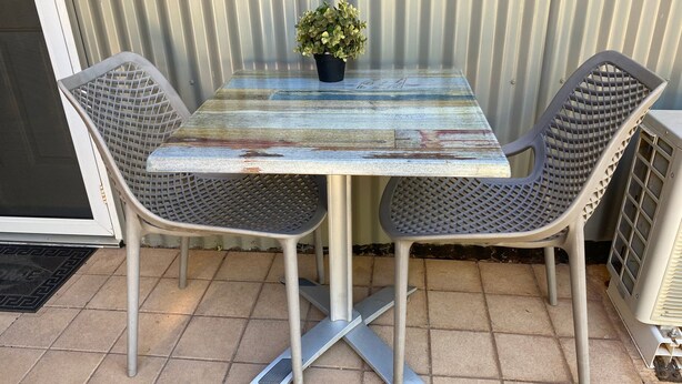A metal table with a distressed paint finish, two metal chairs with a grid pattern, and a potted plant on the table. - Getaway Villas Unit 38-11 - comfort on a budget (EXMOUTH)