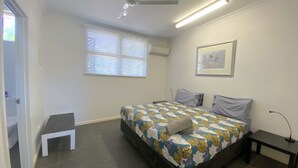 A bedroom with a bed, two pillows, a bedside table, a small white bench, a window with blinds, and a ceiling fan. - Getaway Villas Unit 38-11 - comfort on a budget (EXMOUTH)