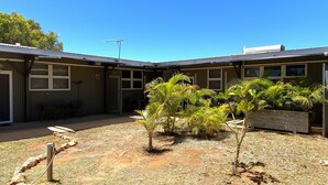 A building with a fenced backyard, a small patio area, and several palm trees.