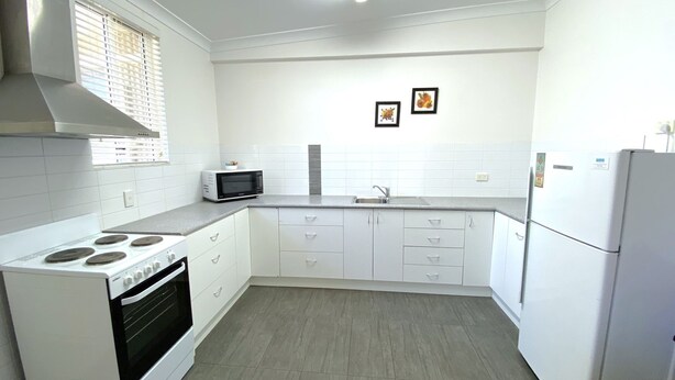 A kitchen with white cabinets, a stove, a microwave, and a refrigerator.