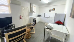 A compact living space with a kitchenette, a dining area, a TV, and a chair with a woven seat.