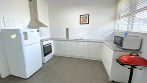 A compact kitchen with white appliances, a microwave, and a red chair.