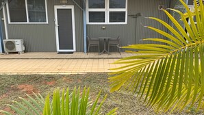 A building with a grey exterior, a door, and two windows. There is a small patio area with two chairs and a table.