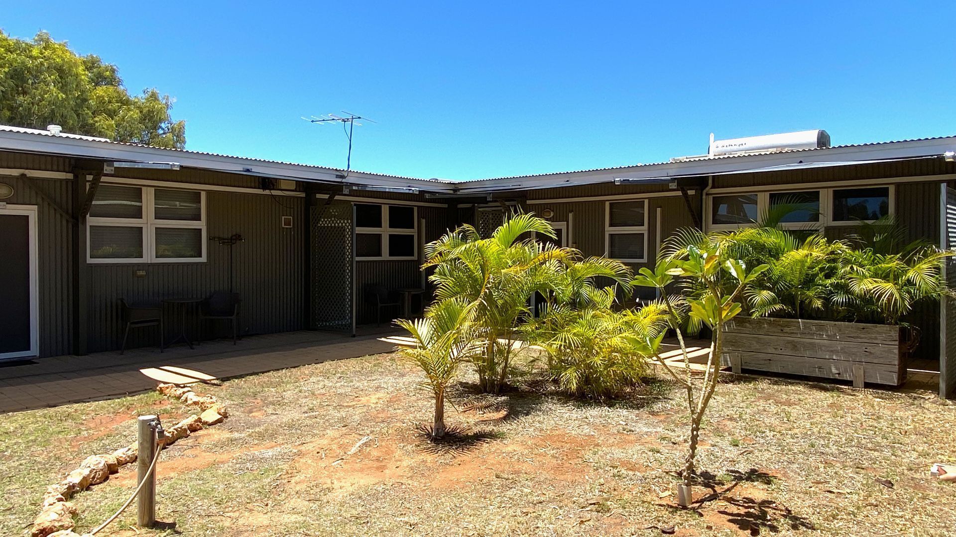 A building with a fenced backyard, a small patio area, and several palm trees.