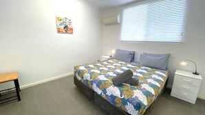 A bedroom with a bed, a bedside table, a lamp, a bench, and a wall-mounted air conditioner.