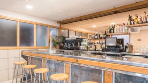 A bar area with a marble countertop, wooden stools, a coffee machine, and shelves with bottles.