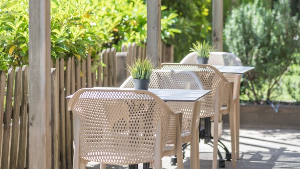 An outdoor patio area with wicker chairs and tables, surrounded by a wooden fence and lush greenery.