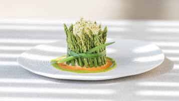Une assiette blanche ornée d’un bouquet d’asperges au centre, agrémentée de jeunes pousses, posée sur une nappe à rayures.