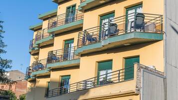 Un edificio de varios pisos con balcones, barandillas verdes y un pequeño jardín.