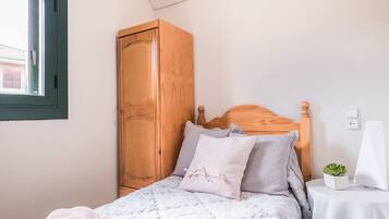 Un dormitorio con un armario de madera, una cama con una manta blanca y una pequeña mesa con una planta.