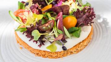 A round, white plate with a slice of cake topped with a colorful salad.