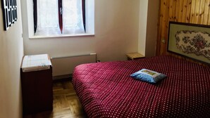 A bedroom with a wooden paneled wall, a window with lace curtains, a bed with a polka dot bedspread, and a framed floral artwork on the wall.
