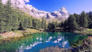 A mountain lake with clear reflections, surrounded by dense forest and rocky mountains.