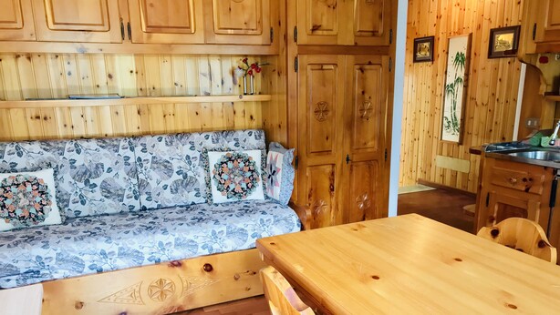 A wooden interior with a sofa, wooden cabinets, and a dining table.