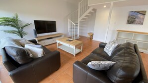 A modern living room with a flat-screen TV, two leather sofas, a wooden coffee table, and a staircase leading to another level.