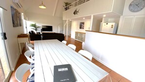 A spacious dining area with a long table, white chairs, and a black folder on the table.