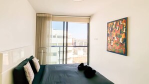 A bedroom with a bed, a window with curtains, and a colorful painting on the wall. - Design Apt Parking Included 2BDR TL30 (Tel Aviv)