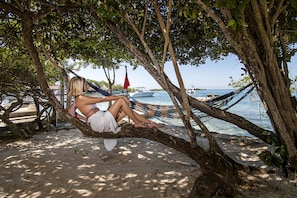 A hammock tied between trees on a sandy beach with boats in the background. - Isla Tijereto (Rosario Islands)