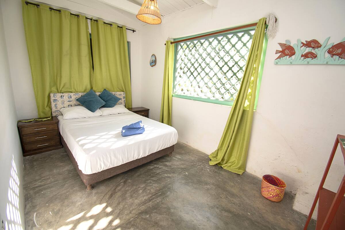 A bedroom with a bed, green curtains, a window with a lattice design, and a wall decoration of fish.