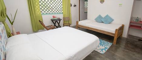 Una habitación con dos camas, una mesita pequeña, una silla, una planta y un ventanal con cortinas verdes.