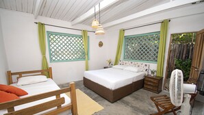 A bedroom with two wooden beds, a wooden chair, a standing fan, and a small table with a plant.