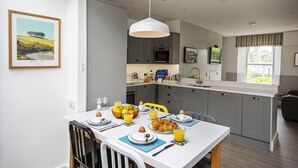 Una cocina moderna con armarios grises, una encimera blanca y un comedor con una mesa dispuesta para el desayuno.
