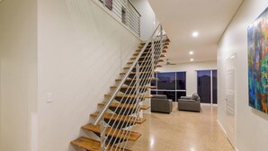 Ein modernes Interieur mit einer Holztreppe, einer Wohnbereits mit Sofas und einem großen, abstrakten Gemälde an der Wand.