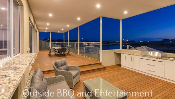 Eine moderne Außenküche mit Grill, Essbereich mit Stühlen und Blick auf die Landschaft im Abendrot.