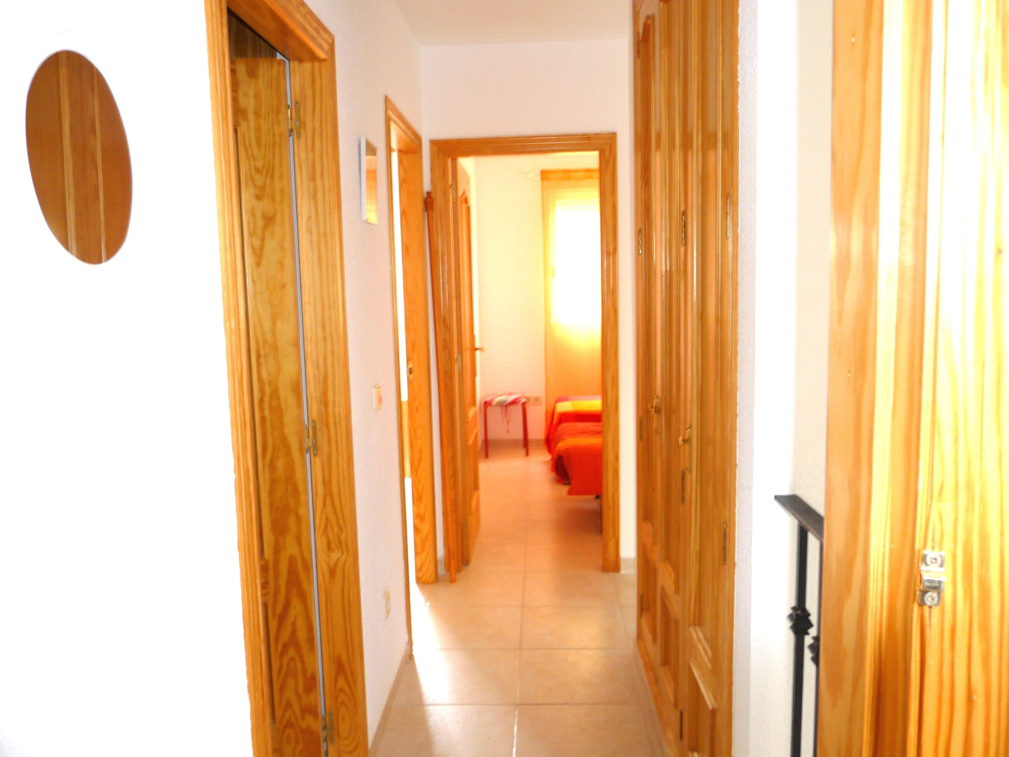 Un pasillo con puertas de madera que dan a una habitación con cama y ventana.