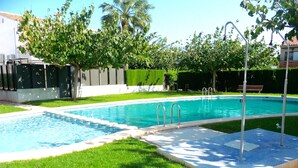Una piscina con bordo piastrellato, circondata da prato e alberi curati.