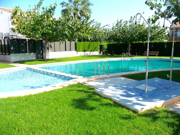 A swimming pool with a tiled deck, surrounded by well-maintained grass and trees.