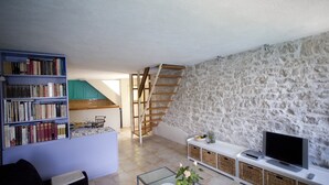 A living room with a stone wall, a bookshelf, a TV, and a staircase.