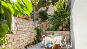 An outdoor patio with a stone wall, a table set for dining, and potted plants.
