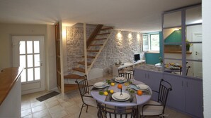 A dining area with a stone wall, a wooden staircase, and a kitchen area with a counter and cabinets.