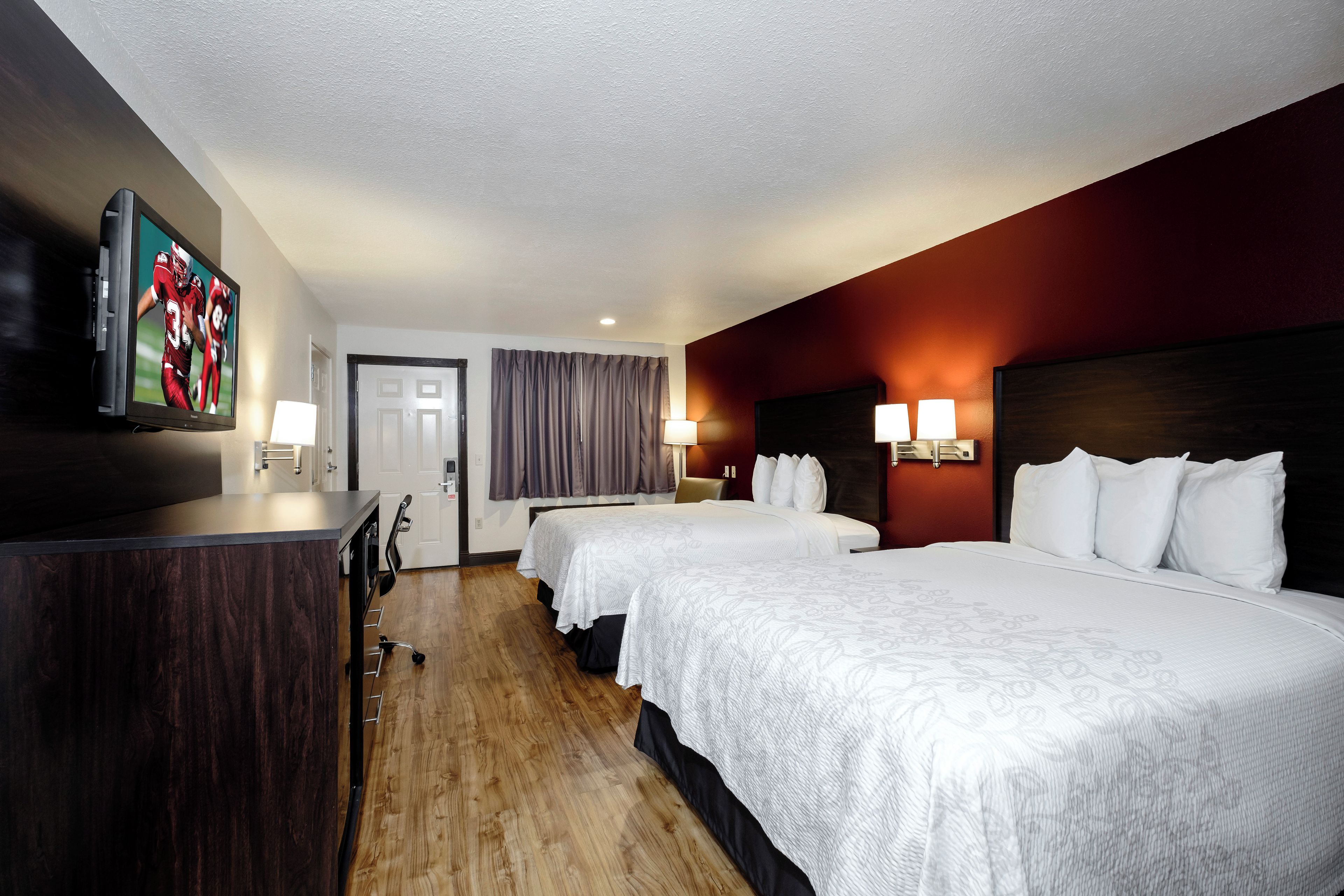 Ein Hotelzimmer mit einem großen Bett, einem Schreibtisch, einem Fernseher und einer Tür.