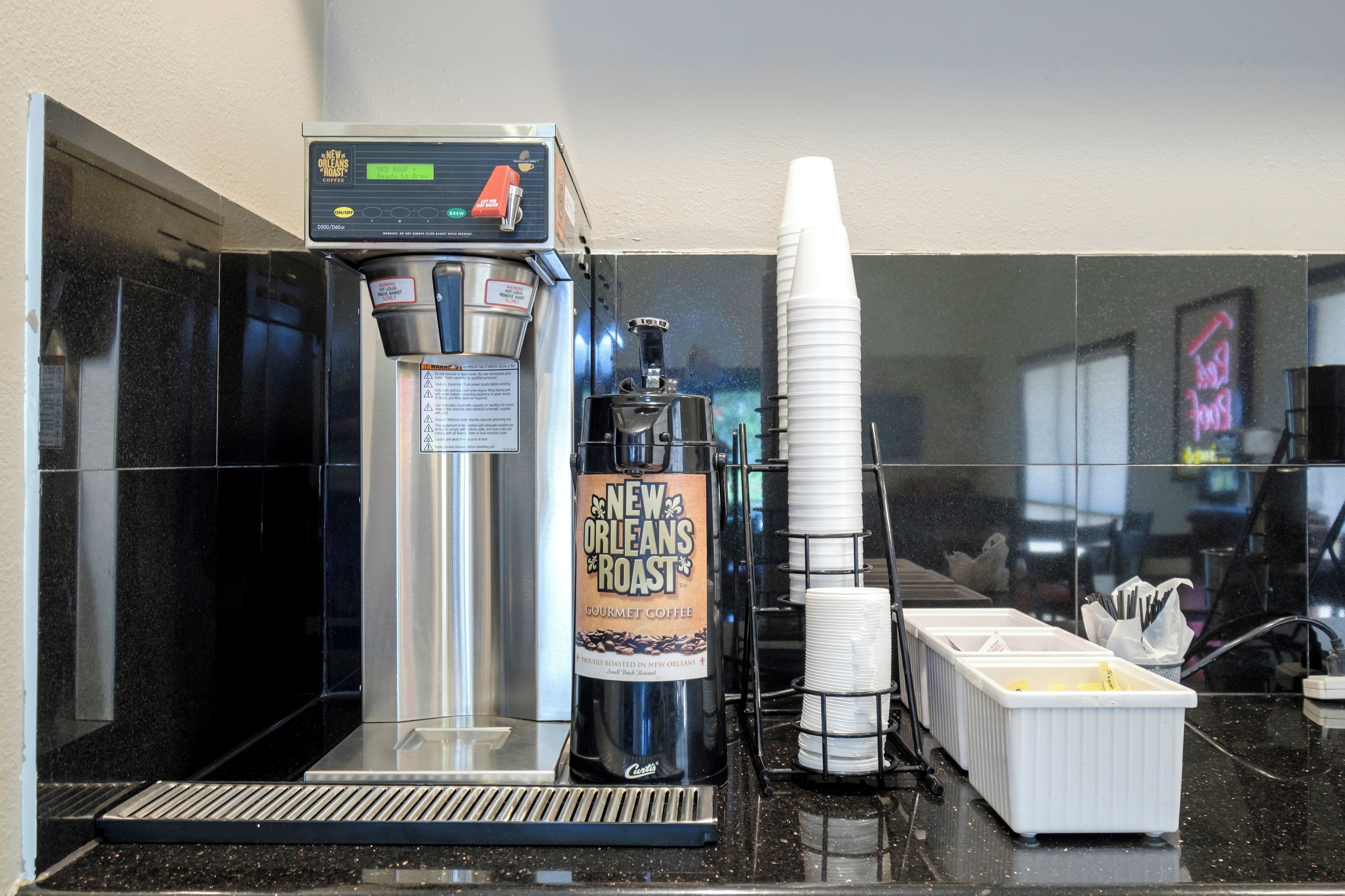 Una cafetera con un rótulo para café New Orleans Roast, una pila de vasos desechables y un dispensador de café.