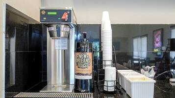 Una cafetera con un rótulo para café New Orleans Roast, una pila de vasos desechables y un dispensador de café.