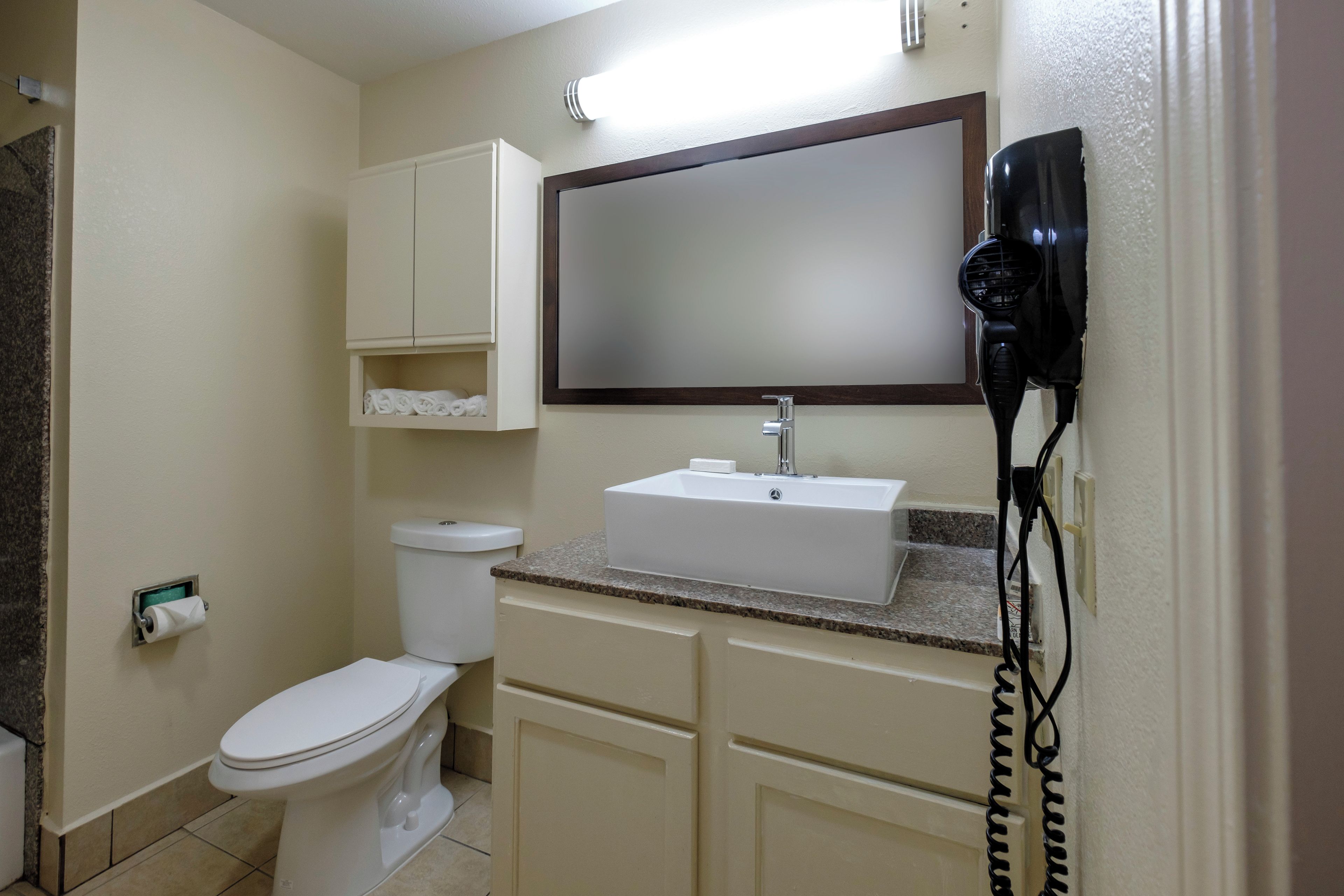 Un baño con inodoro, lavabo, espejo y secador de pelo.