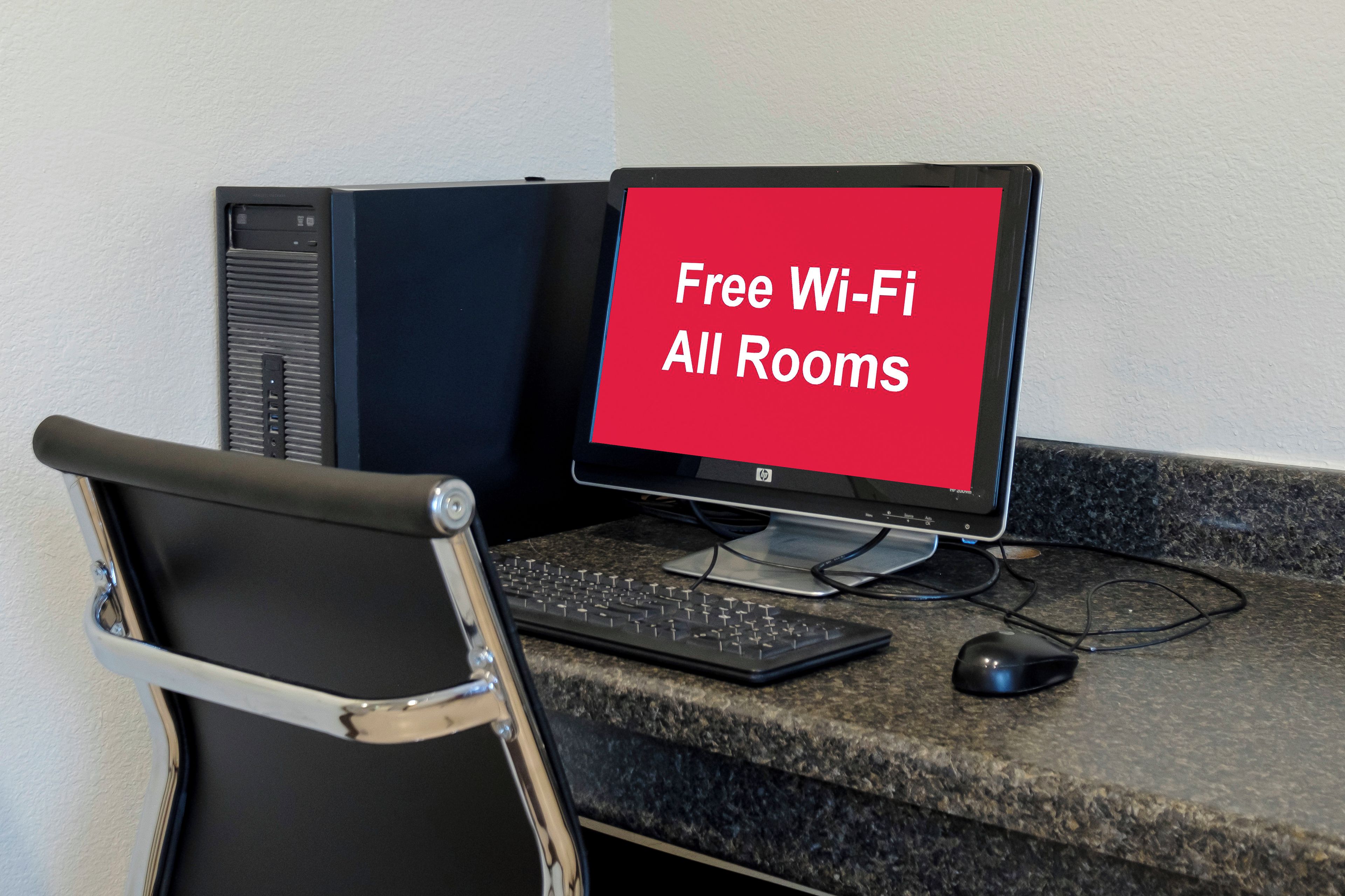Un ordinateur de bureau avec un écran affichant le texte « Wi-Fi gratuit dans toutes les chambres », un clavier, une souris et une chaise.