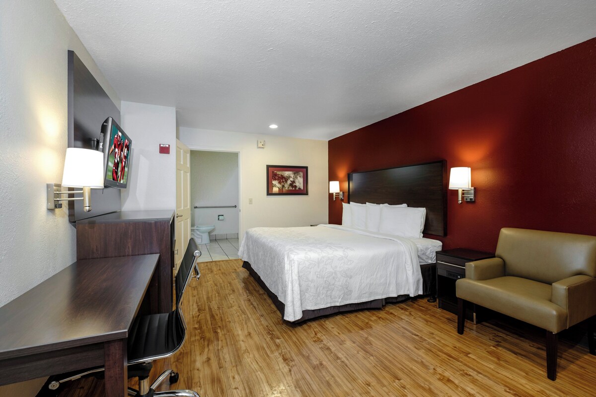 A hotel room with a bed, a desk, a chair, a TV, and a bathroom.