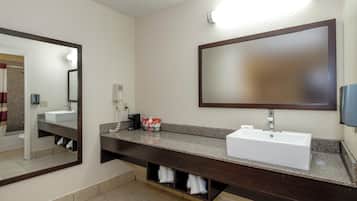 Un baño de hotel con un espejo grande, un lavamanos, un perchero para toallas y una cafetera.