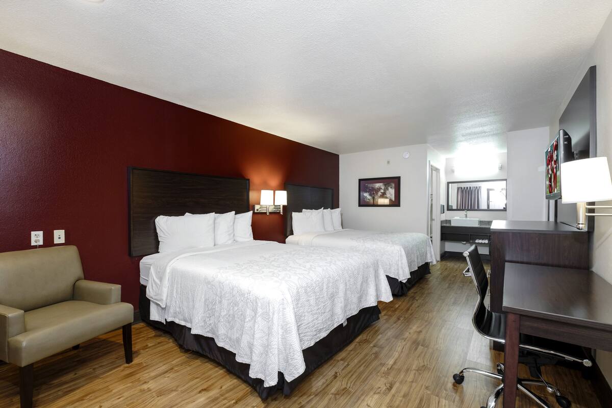 A hotel room with two beds, a desk, a chair, and a TV.
