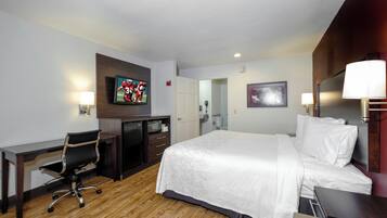 Habitación de hotel con cama, escritorio, silla, televisor y baño visible a través de una puerta abierta.
