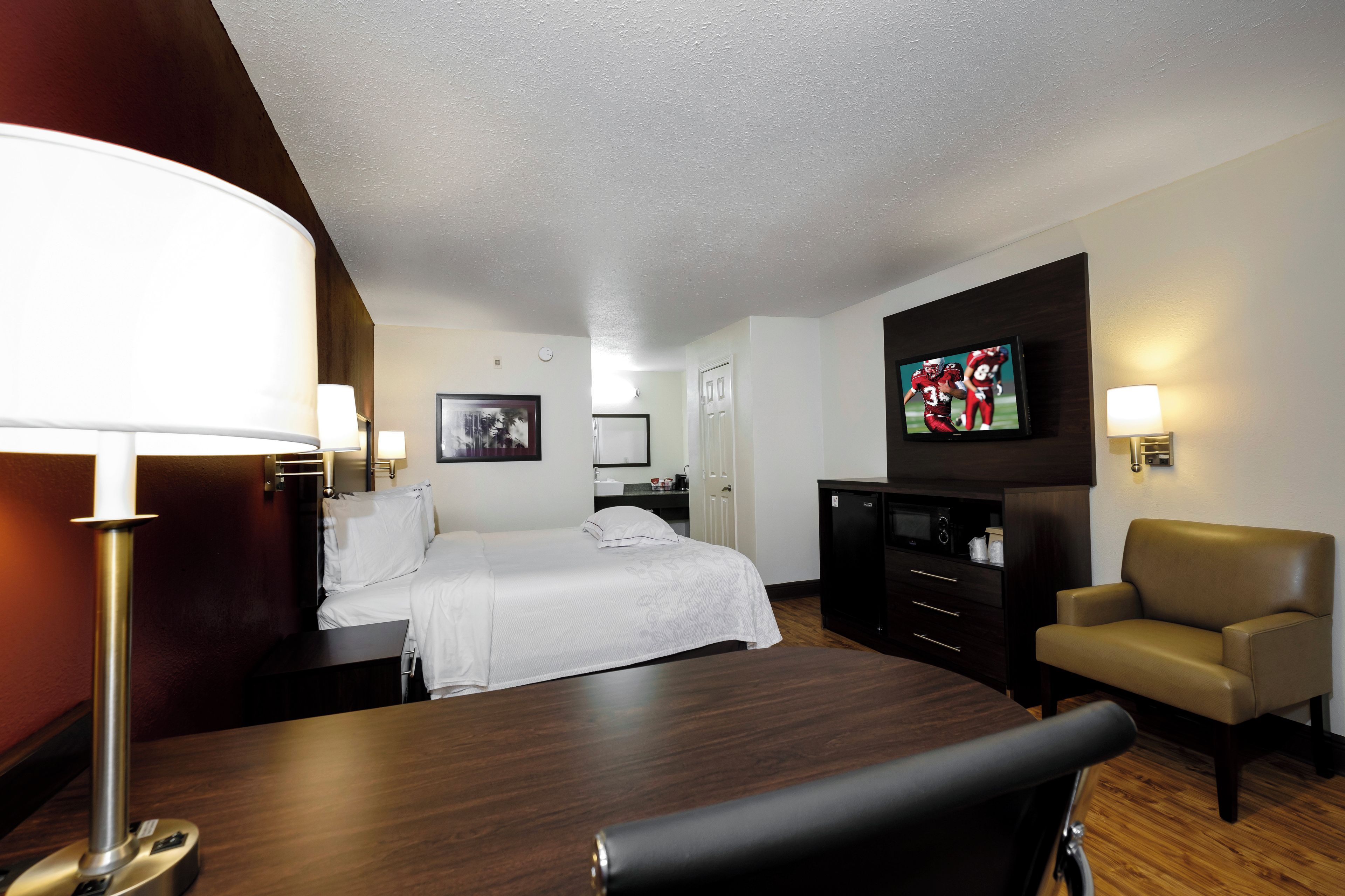 Ein Hotelzimmer mit einem Bett, einem Schreibtisch, einem Sessel, einem Fernseher und einer Schreibtischlampe.
