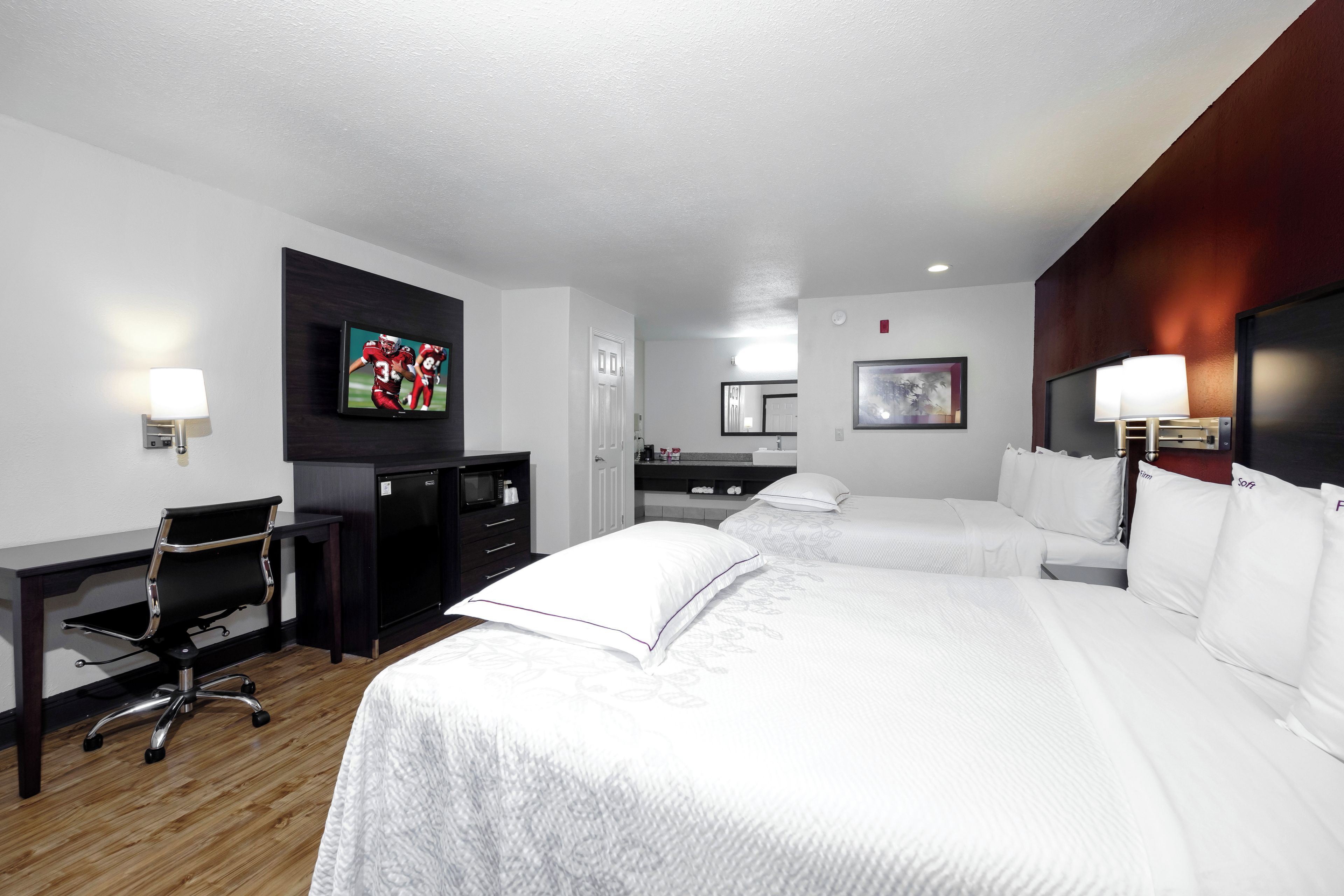 A hotel room with two beds, a desk, a TV, a microwave, and a bathroom.